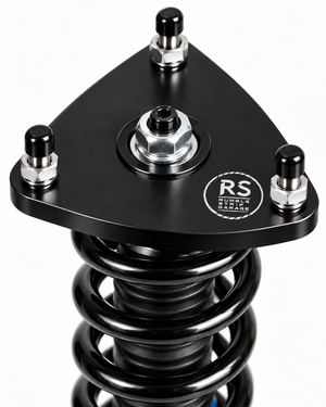 A close-up studio shot of a black automotive shock absorber assembly with a triangular mounting plate, silver hardware, and a visible RS Performance Garage logo on the plate, set against a plain white background.